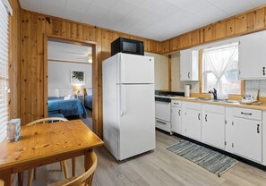 A kitchen with wooden walls, a white refrigerator, a stove, and a dining area with a table and chairs.