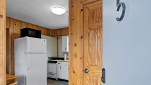 A compact kitchen with a refrigerator, stove, and wooden cabinets. - Snug Harbor Inn | Blueberry Suite | Near Lake MI (Muskegon)