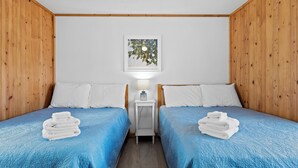 A room with two beds, white pillows, a small bedside table with a lamp, and a framed picture on the wall. - Snug Harbor Inn | Blueberry Suite | Near Lake MI (Muskegon)