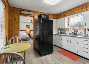 Una cocina con refrigerador negro, armarios de madera, una mesa de comedor con sillas y una ventana con vistas.