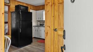 A kitchen with wooden cabinets, a black refrigerator, and a microwave. - Snug Harbor Inn | The Roost | Near Lake MI (Muskegon)