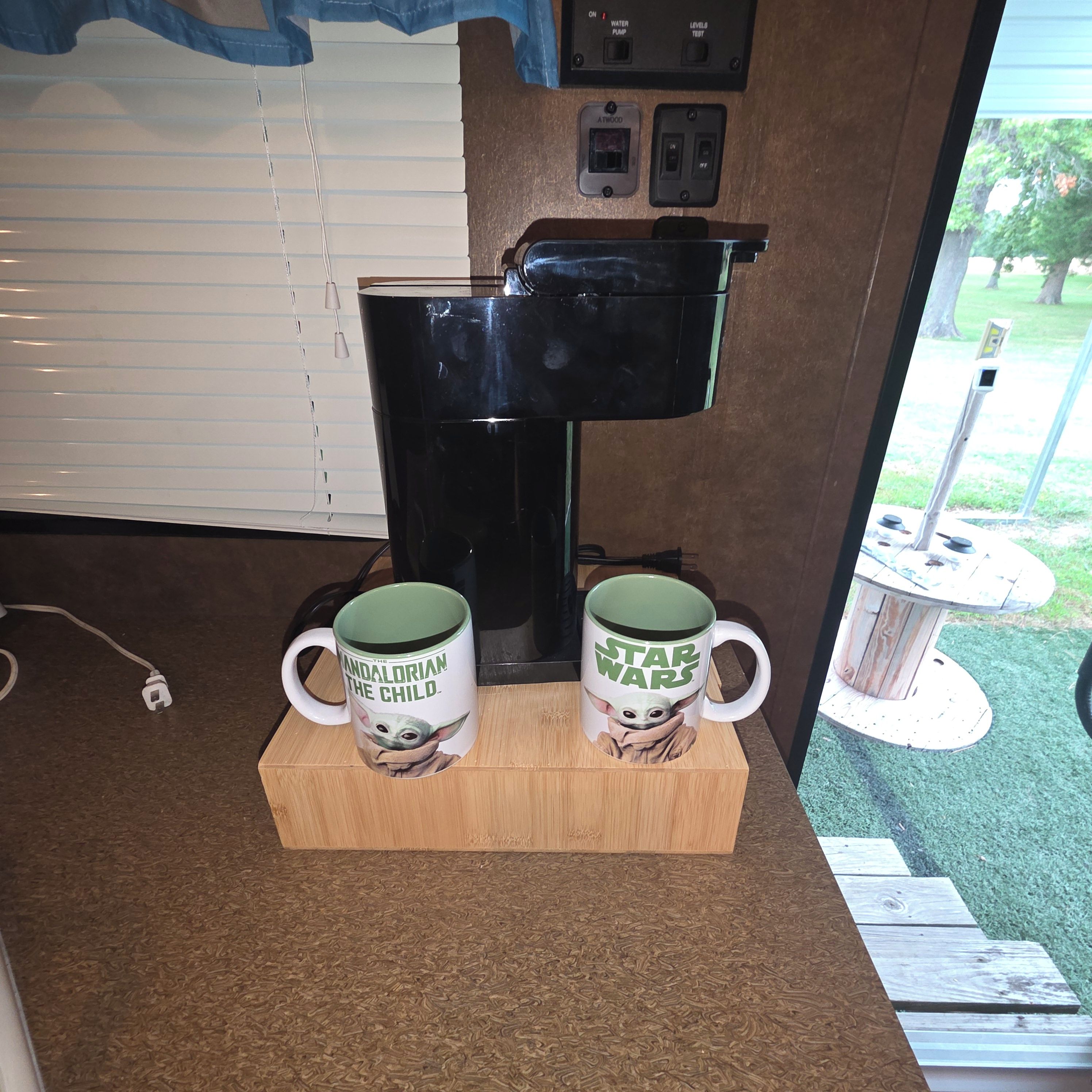 Een koffieapparaat met twee mokken op een houten voetstuk.
