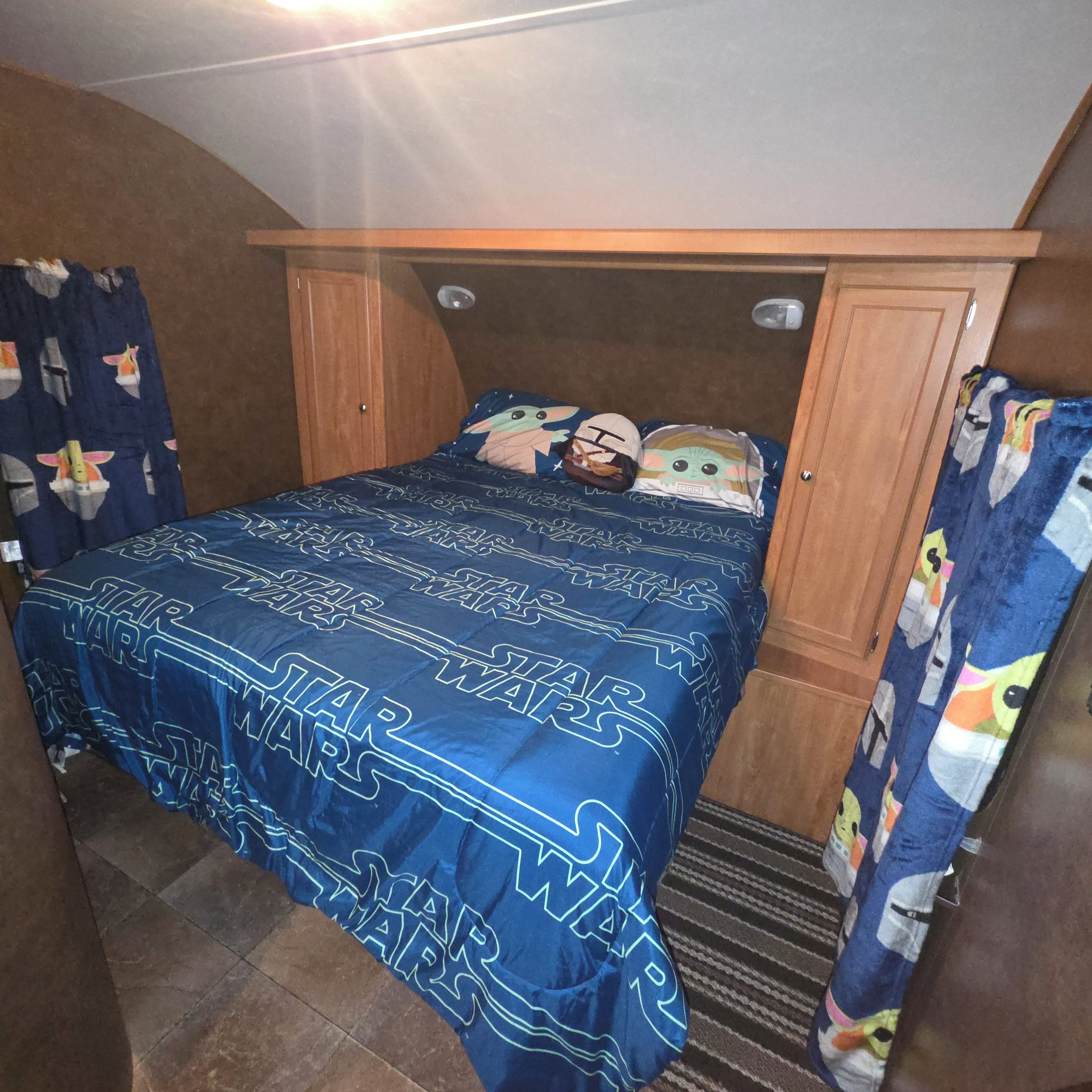 Een slaapkamer met een Star Wars bedsprei, een houten hoofdbord en een gordijn met een stripfiguren ontwerp.