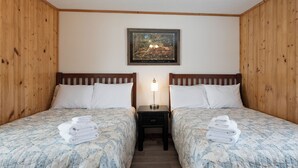 Een kamer met twee bedden, een nachtkastje met een lamp en een schilderij aan de muur.