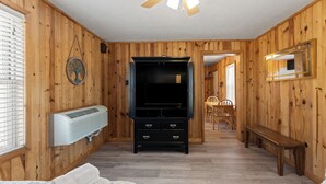 Een kamer met houten lambrisering, een bed, een bankje, een televisie, een verwarming en een eethoek.