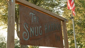 Une enseigne en bois rustique portant l’inscription « The Snug Harbor Inn ».