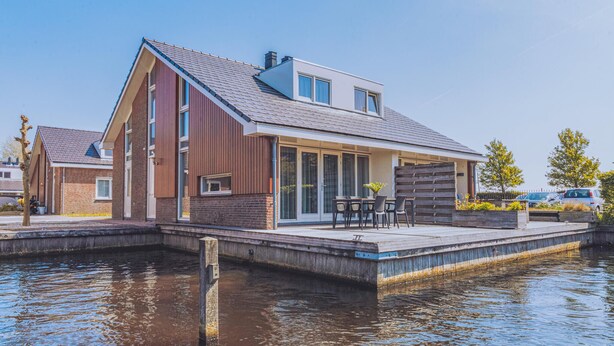 A modern house with a sloped roof, large windows, and a dock extending into a body of water. - Dorregeest kalender 1 (Uitgeest)