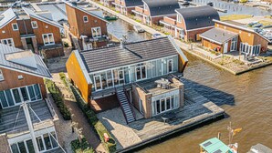 Un moderno housebot con tetto piatto, ampie finestre e un pontile che si protende in un canale.