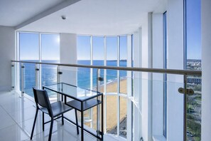 Ein Hotelzimmer in einem Hochhaus mit einem Glasbalkon und Blick auf Strand und Meer.