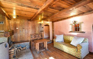 A rustic cabin interior with wooden walls, a stone fireplace, a wooden table, a sofa, and a window with a wooden frame. - Amazing apartment in Cogne (Cogne)