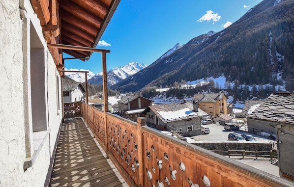 A balcony with a wooden railing overlooking a village with snow-covered roofs and mountains in the background. - Amazing apartment in Cogne (Cogne)