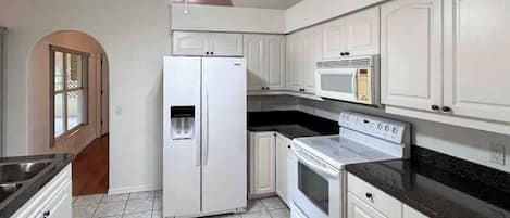 A kitchen with white cabinets, a refrigerator, a microwave, and a stove.