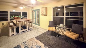 Un coin repas avec une table et des chaises en bois, un ventilateur de plafond et une grande fenêtre.