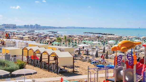 A beach with rows of sunbeds and umbrellas, a playground, and a view of the sea and buildings in the distance. - 1 bedroom nice apartment in Cattolica (Cattolica)