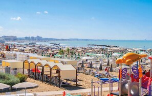 A beach with rows of sunbeds and umbrellas, a playground, and a view of the sea and buildings in the distance. - 1 bedroom nice apartment in Cattolica (Cattolica)