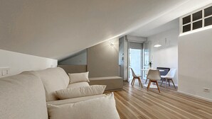 A modern loft bedroom with a built-in sofa, a dining area with a table and chairs, and a large window providing natural light. - 1 bedroom nice apartment in Cattolica (Cattolica)