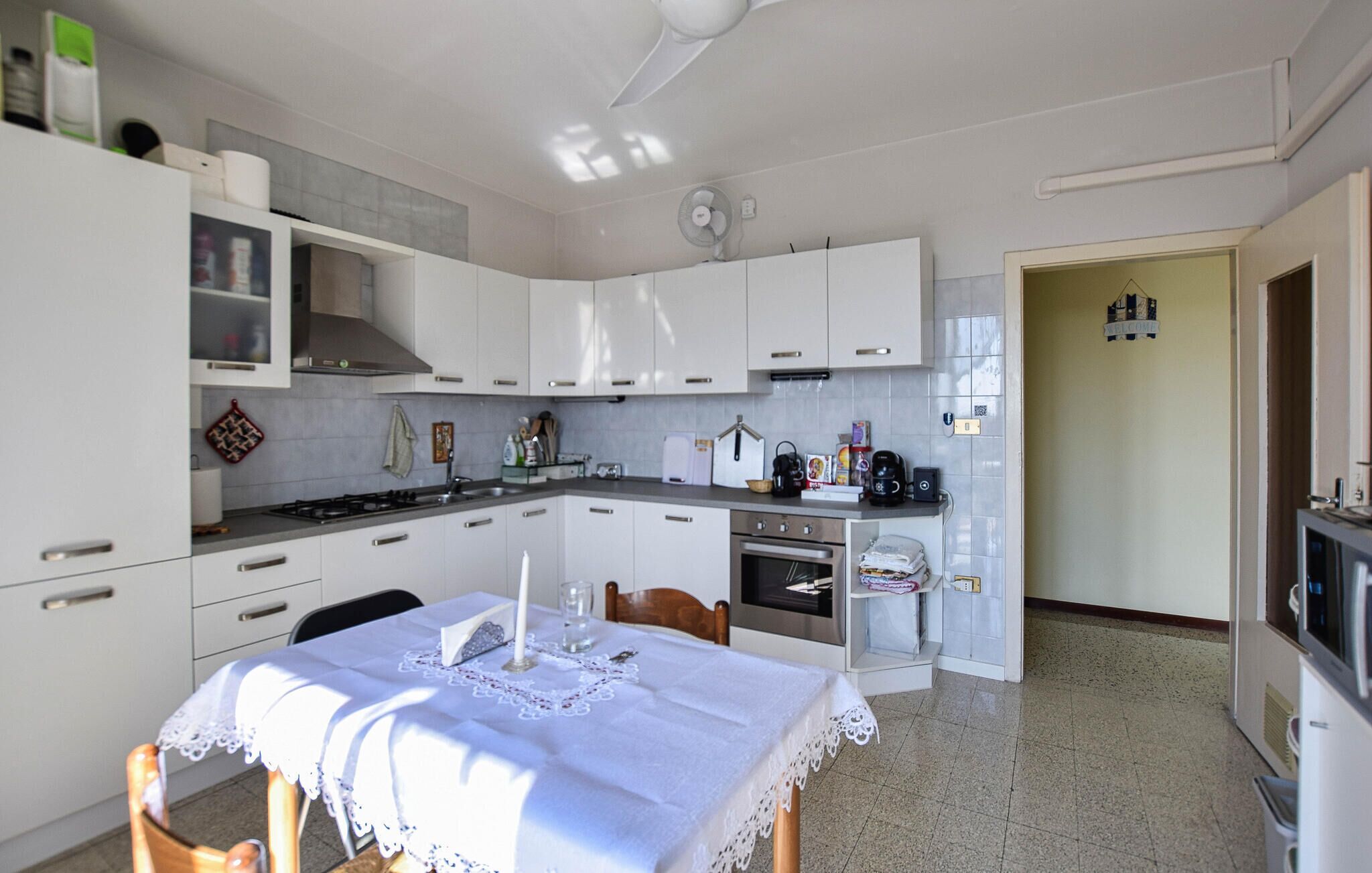 A kitchen with white cabinets, a dining table with a lace tablecloth, and a TV in the corner.