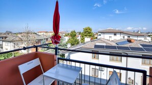 En balkon med et bord og stole, en rød parasol og solpaneler på taget.