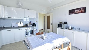 Et moderne køkken med hvide skabe, et spisebord med hvide blonde og en mikrobølgeovn samt en ventilator i loftet.