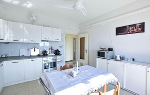 Eine moderne Küche mit weißen Schränken, einem Esstisch mit Spitzenleinentuch, einer Mikrowelle und einem Deckenventilator.