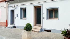 Ein Gebäude mit drei Fenstern und drei Türen, einem kleinen Garten und der Hausnummer 134 an der Wand.