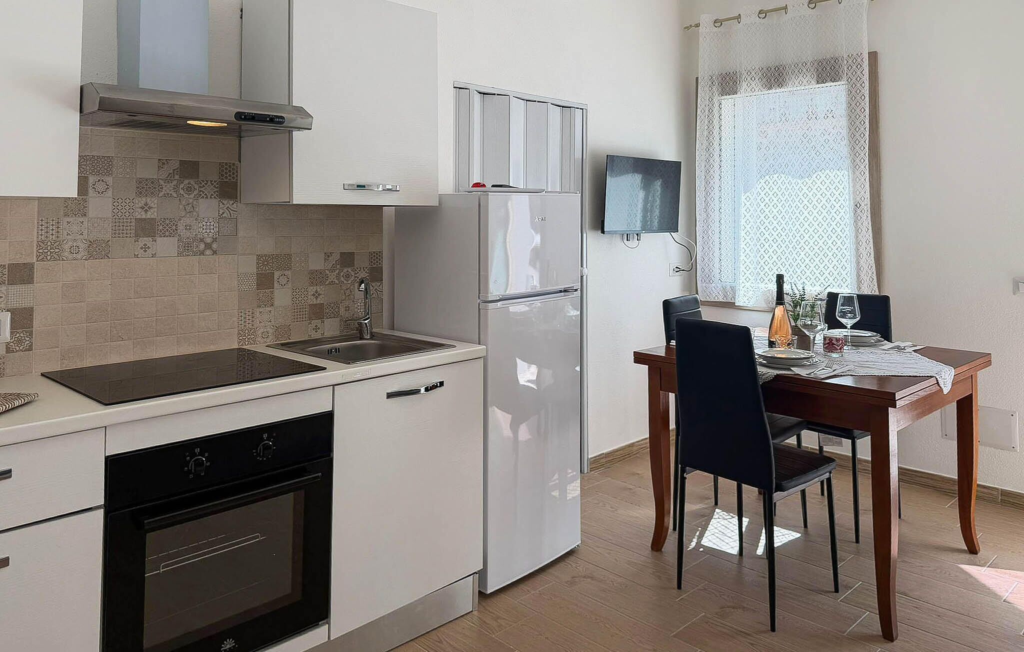 Eine kompakte Küche mit Herd, Backofen, Spüle und Kühlschrank. Es gibt eine Essecke mit Tisch und Stühlen.