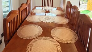 A dining table with a wooden finish, surrounded by wooden chairs, set with woven placemats, and a view of a mountainous landscape through a window. - Cozy Villa Mountain View Cold Weather in Marilog Perfect for Relaxing getaways (Arakan)