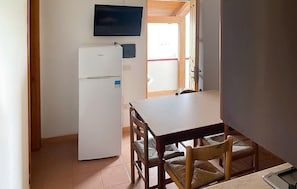 A compact kitchen with a refrigerator, a dining table with chairs, and a television mounted above the counter. - 2 bedroom lovely apartment in Ricadi (Ricadi)