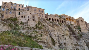 Un edificio storico con diversi livelli, finestre ad arco e balconi, situato su una scogliera ripida.
