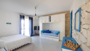 Una camera da letto con un letto, una poltrona, una scrivania e una scacchiera, e un muro in pietra.