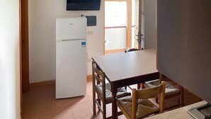 A compact kitchen with a refrigerator, a dining table with chairs, and a television mounted above the counter. - Nice apartment in Ricadi with WiFi (Ricadi)