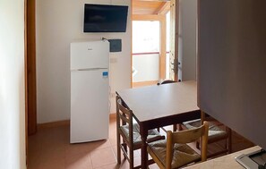 Una cocina compacta con refrigerador, una mesa de comedor con sillas y un televisor sobre la encimera.