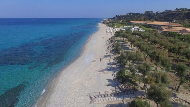 A coastal beach with a paved walkway, trees, and buildings in the background. - Nice apartment in Ricadi with WiFi (Ricadi)