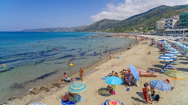 Una playa con agua cristalina, sombrillas y gente.
