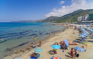Ein Strand mit klarem Wasser, Sonnenschirmen und Menschen.