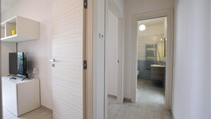 Un pasillo con un mueble para televisión, una puerta y un baño a la vista a través de otra puerta abierta.
