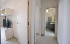 A hallway with a TV stand, a door, and a bathroom visible through an open door. - Awesome apartment in Ascea (Ascea)