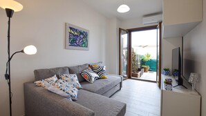 Una sala de estar moderna con un sofá gris, cojines estampados, un cuadro y vistas al exterior.