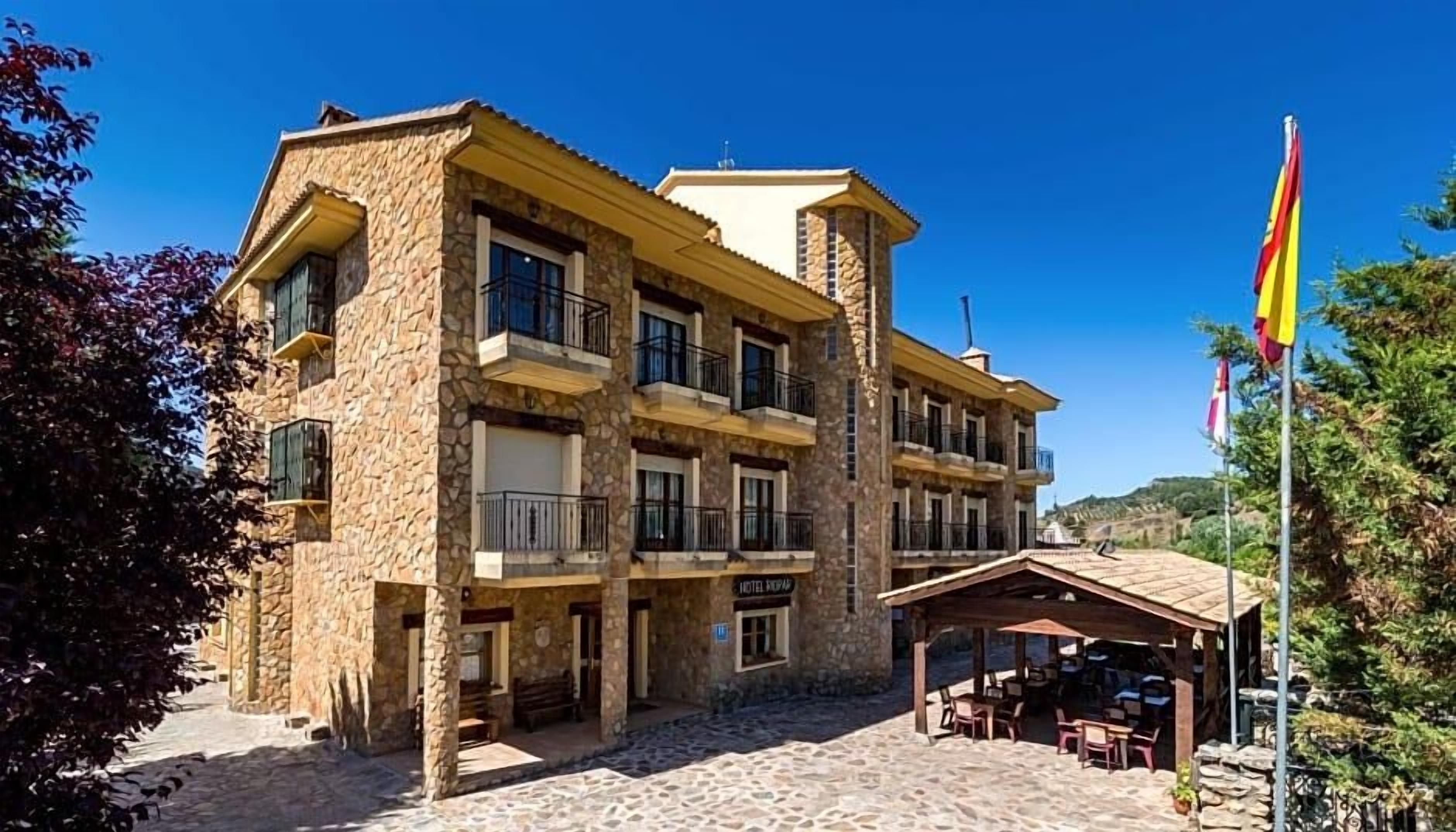 Un edificio de varios pisos de piedra con balcones, un área de estar al aire libre cubierta y una bandera.