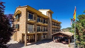 A multi-story stone building with balconies, a covered outdoor seating area, and a flag. - Hotel Riopar Spa (Riopar)