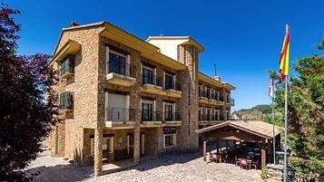 Un edificio de varios pisos de piedra con balcones, un área de estar al aire libre cubierta y una bandera.