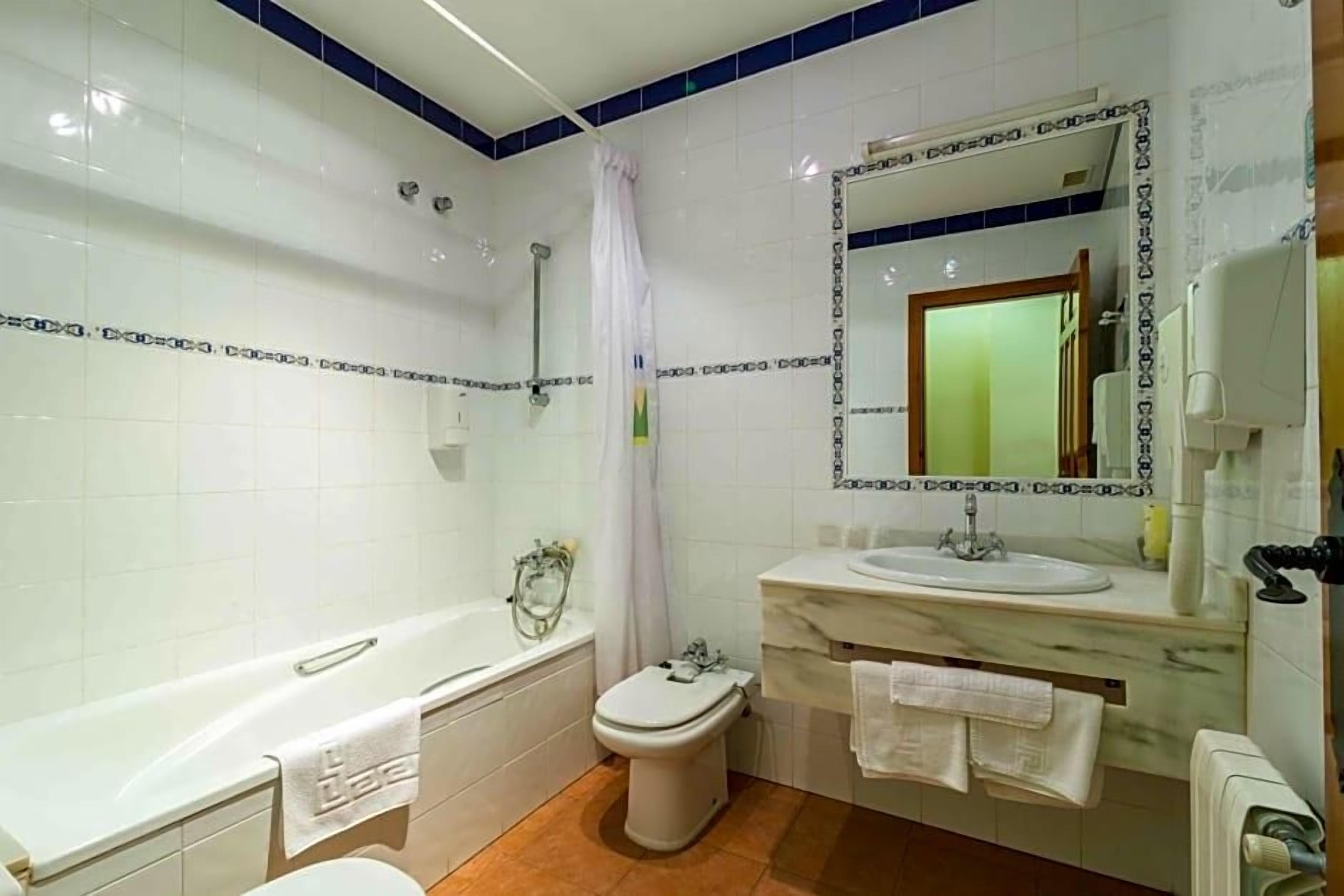 Un baño con bañera, inodoro y lavamanos, con azulejos blancos y una pared de acento azul.