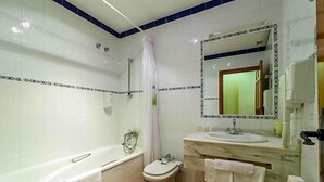 A bathroom with a bathtub, toilet, and sink, with white tiles and a blue accent wall. - Hotel Riopar Spa (Riopar)
