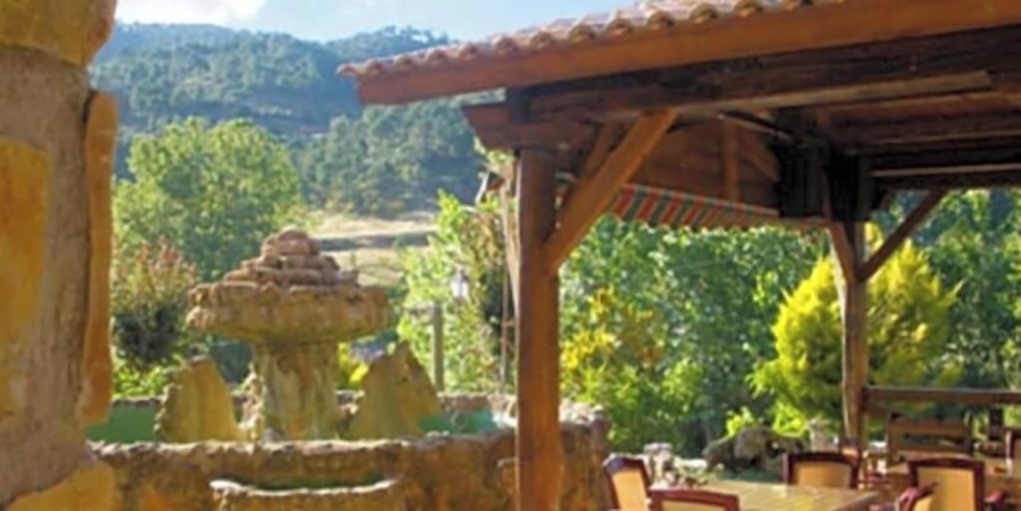 Zona exterior coberta amb una font de pedra, una pèrgola de fusta i taules amb caires.