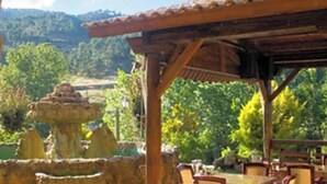 A covered outdoor area with a stone fountain, wooden pergola, and tables and chairs. - Hotel Riopar Spa (Riopar)