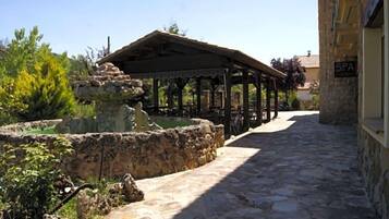 Un camino de piedra conduce a un espacio al aire libre cubierto, con una fuente, un letrero de spa y vegetación.