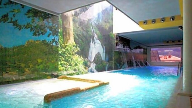 An indoor swimming pool with a waterfall feature and a mural of a forest scene. - Hotel Riopar Spa (Riopar)