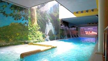 Una piscina interior con caída de agua, rodeada por un mural de un paisaje boscoso.