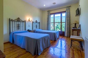 A room with two beds, a window with curtains, a radiator, and a small table with a lamp. - Hotel Riopar Spa (Riopar)