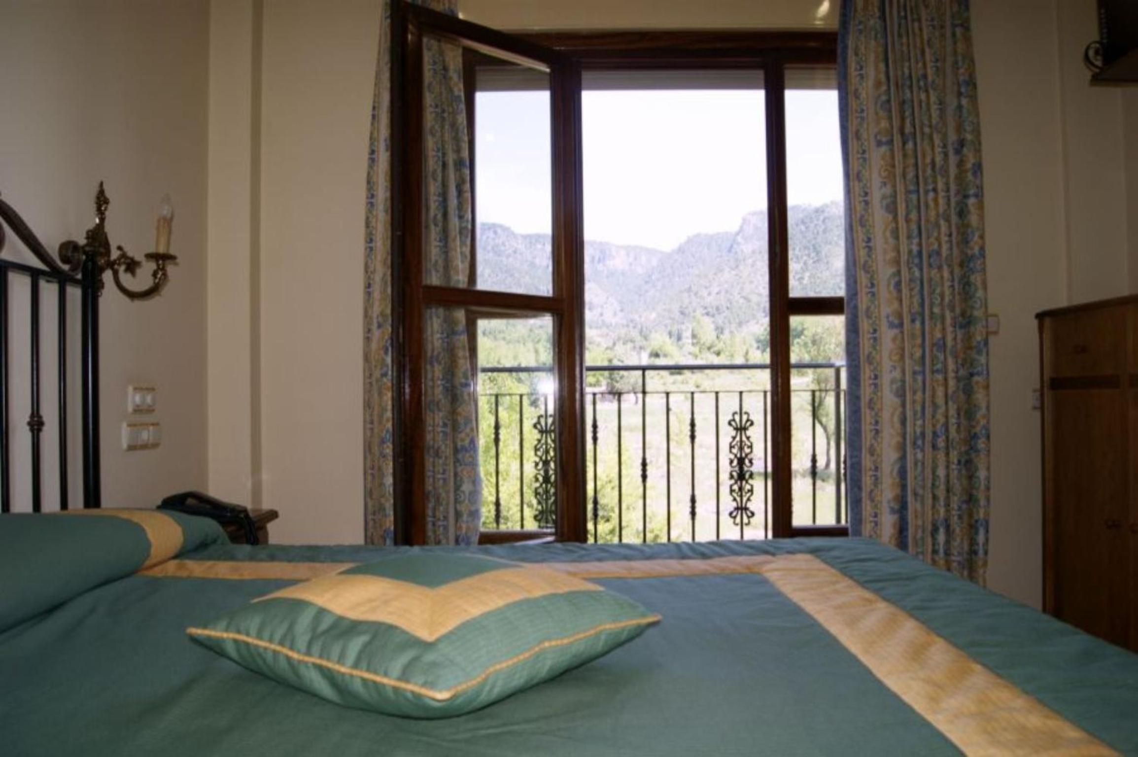 Un dormitorio con cama, mesita de noche, cómoda y balcón con vistas a montañas.